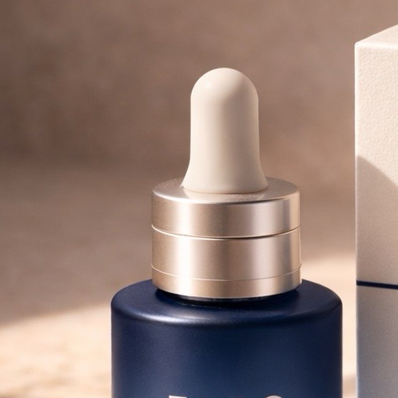 Close-up of the FARO Perial Serum dropper: champagne metal collar and matte ivory bulb on the navy bottle