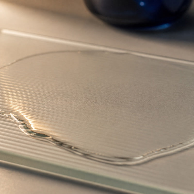 A thin clear serum veil settling evenly across finely textured frosted glass