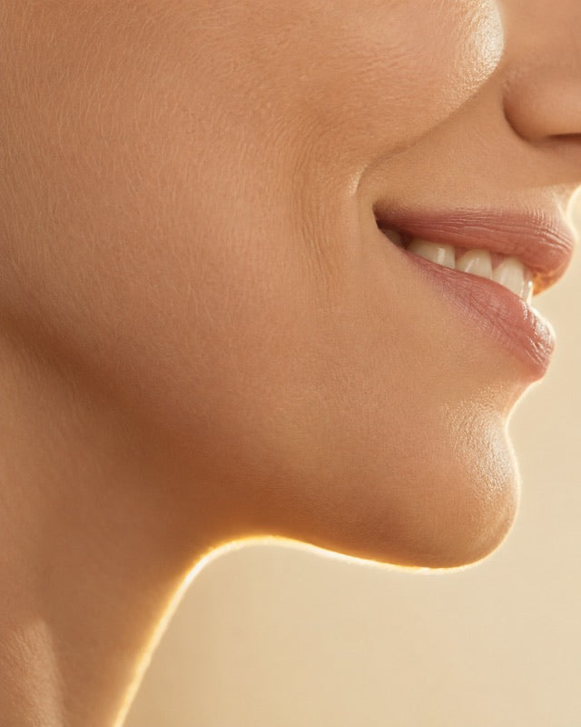 Profile of a smile showing the natural fold of skin at the mouth corner and jawline, backlit in champagne light