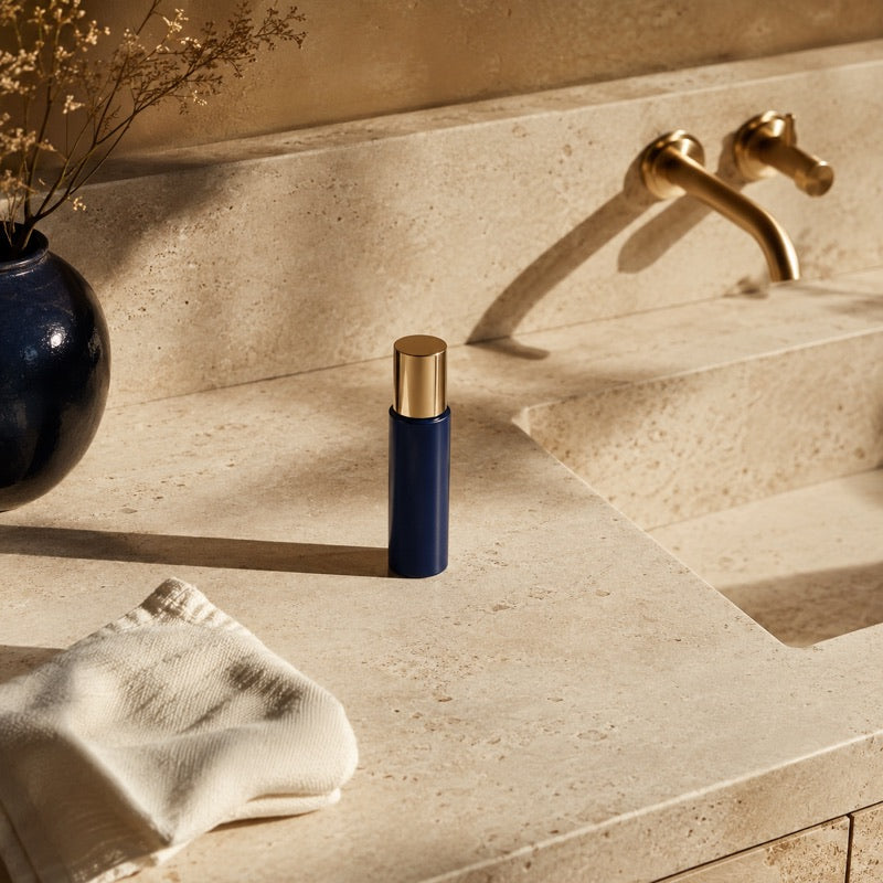 A tidy cream stone counter with the capped navy serum bottle and a folded ivory towel in morning light